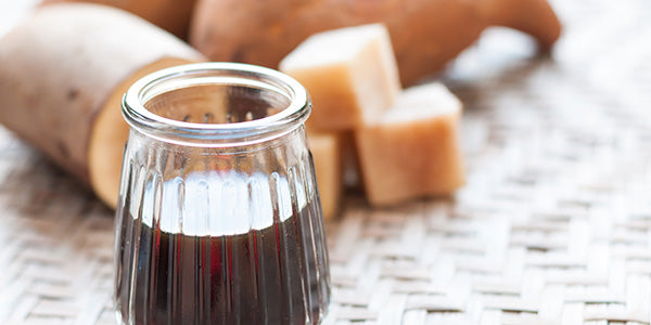 Yacon-Sirup im Glas mit Wurzel im Hintergrund