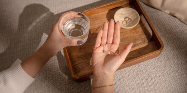 Hand mit Eisenkapsel & Glas Wasser