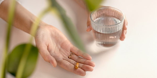 Hand mit Kurkuma-Kapsel und Wasserglas