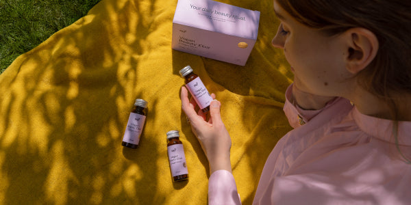 Frau mit Vegan Beauty Elixir im Park auf gelber Decke
