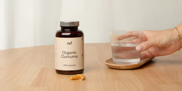 Kurkuma Dose neben Frauenhand - nimmt Kapseln mit Wasser