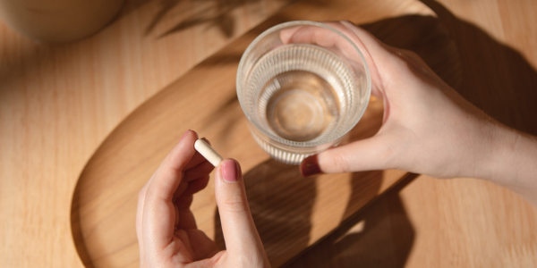 Hand mit Vitamin-C-Kapsel & Glas Wasser