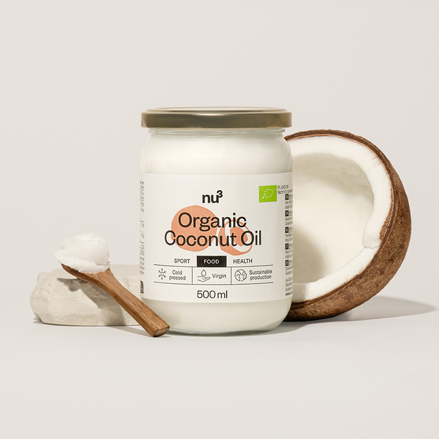 Kokosöl von nu3 neben halber Kokosnuss und Holzlöffel mit Öl