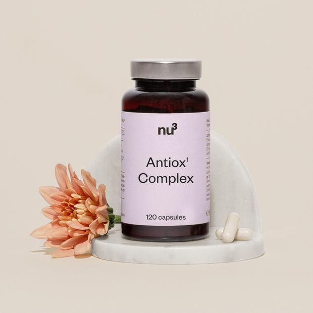 Antiox Complex mit orangefarbener Blume und zwei Kapseln auf Mamor