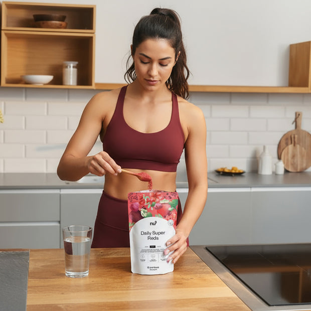 Frau in der Küche nimmt einen Löffel Daily Super Reds mit einem Glas Wasser auf dem Tisch