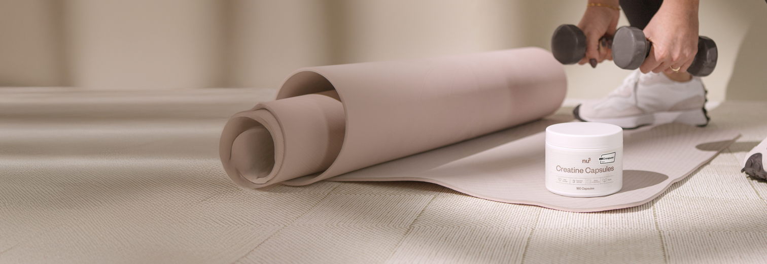 Creatin-Verpackung auf Yogamatte steht vor Person mit Hanteln