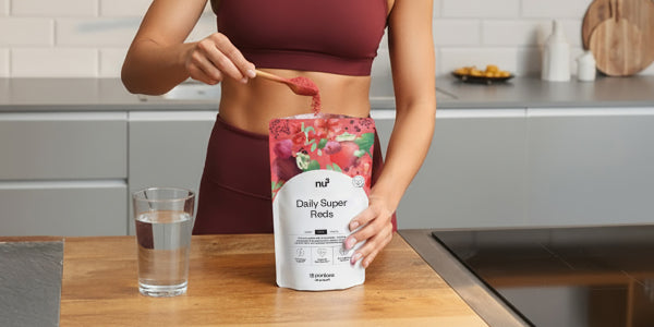 Frau nimmt einen Löffel Daily Super Reds daneben ein Glas Wasser