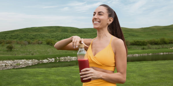 Frau auf grüner Wiese mit rotem Shake in der Hand