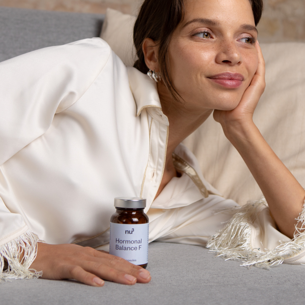 Frau liegend auf dem Bett mit Hormonal Balance Dose in der Hand