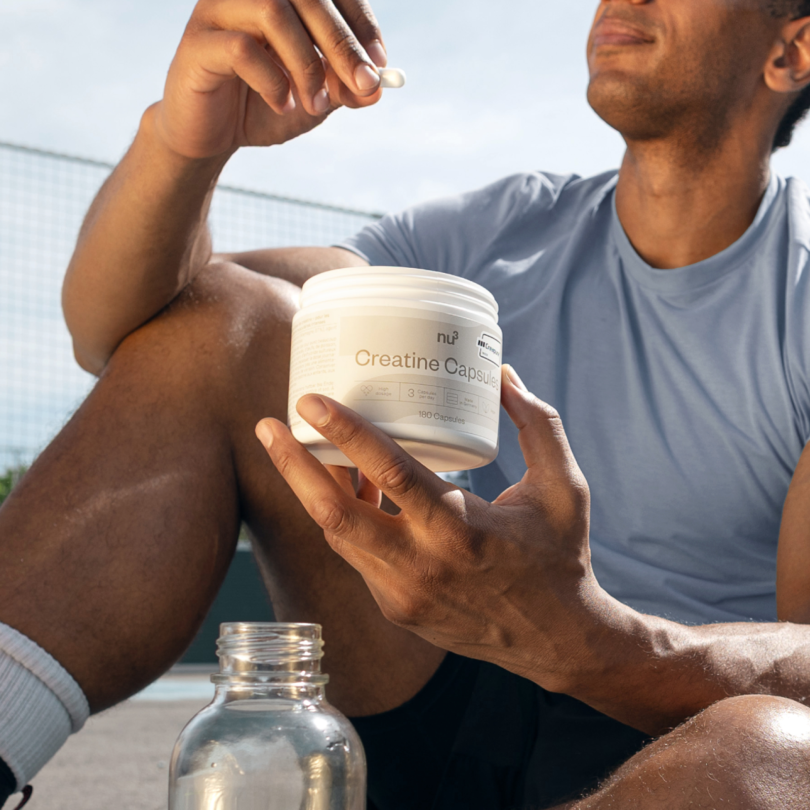 Sportlicher Mann sitzt auf dem Boden und hält Creatine Kapseln
