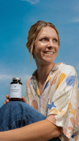 Frau  mit bunter Bluse lächelt und hält nu3 Magnesium Complex