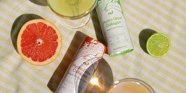 zwei Dosen Hydro Glow Collagen auf gelb gestreifter Tischdecke mit Gläsern, aufgeschnittener Grapefruit und Limette