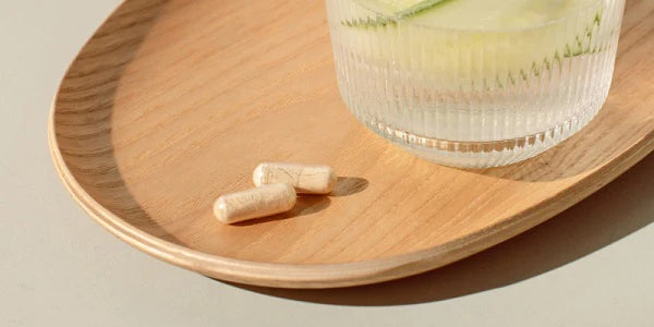 Vitamin C Kapseln neben Glas Wasser auf Holzbrett